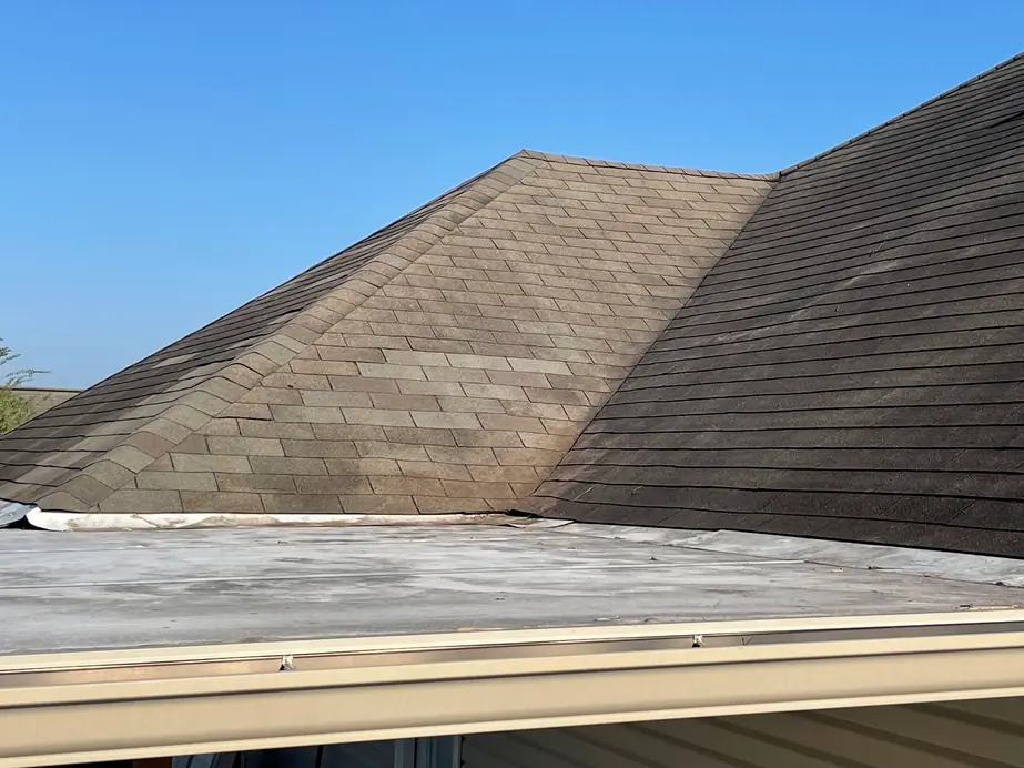 Weathered asphalt shingles meeting a low flat roof section and gutter, ready for repair
