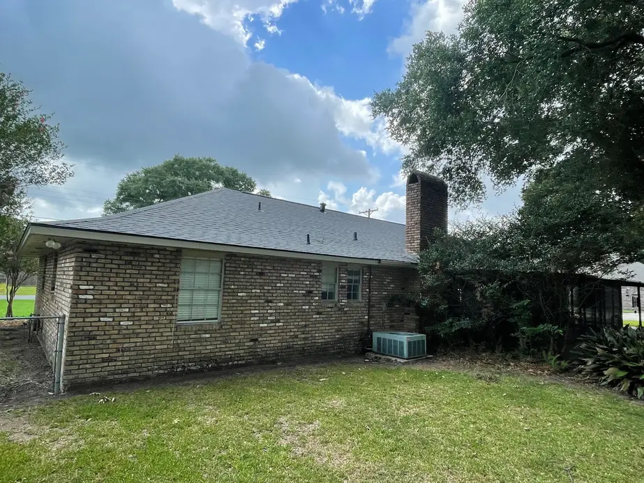 Rear of a brick home with a finished gray shingle roof and chimney