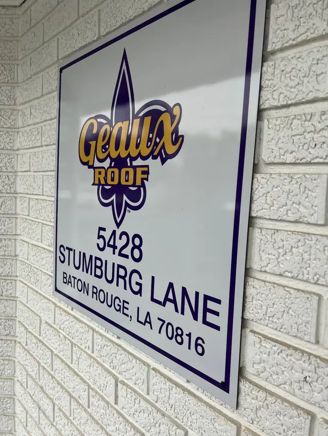 Geaux Roof office sign with the company logo and address on white brick