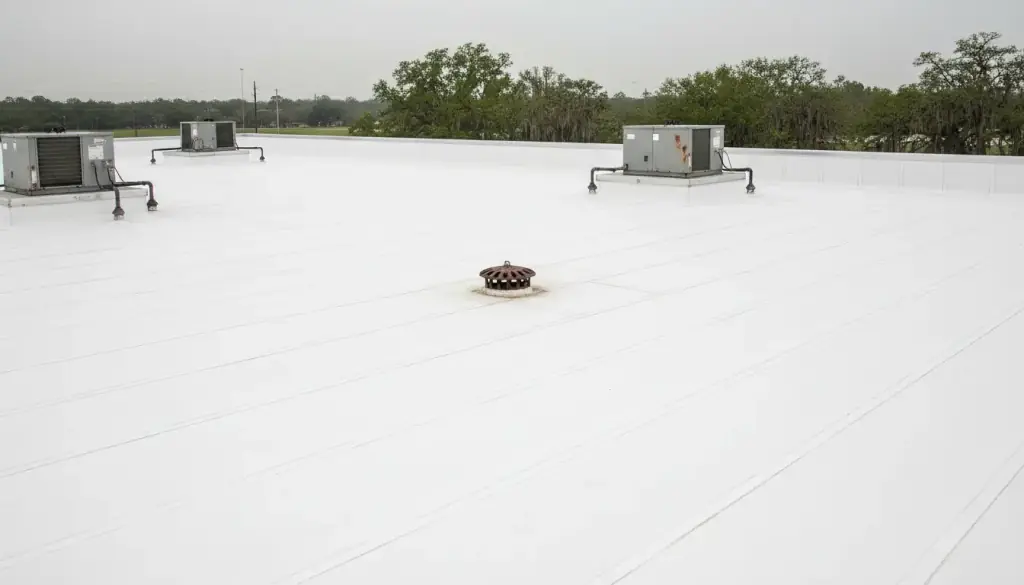 Low-slope white membrane roof on a commercial building with rooftop units and a roof drain