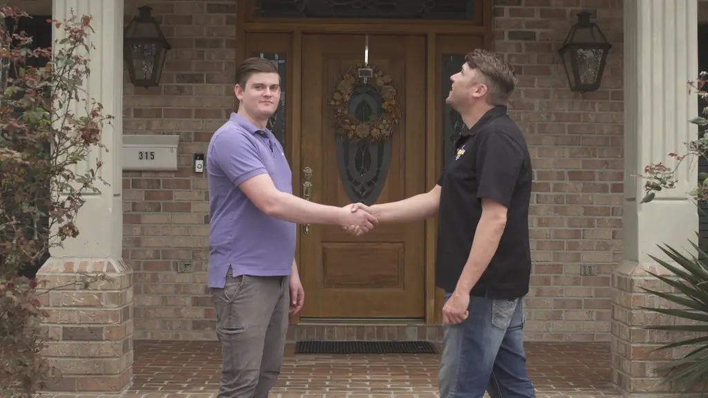 Two men shaking hands on a brick porch, one in a black Geaux Roof fleur-de-lis polo